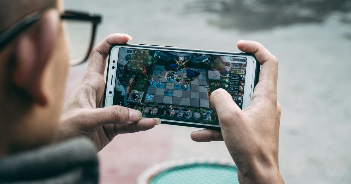 Una persona con lentes sostiene un celular en horizontal con un juego de estrategia en pantalla.