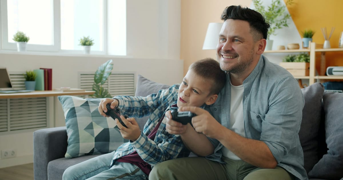 Un padre y su hijo juegan juntos con controles en el sofá.