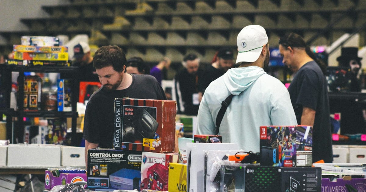 Personas revisan consolas de videojuegos usadas en un puesto de mercado.