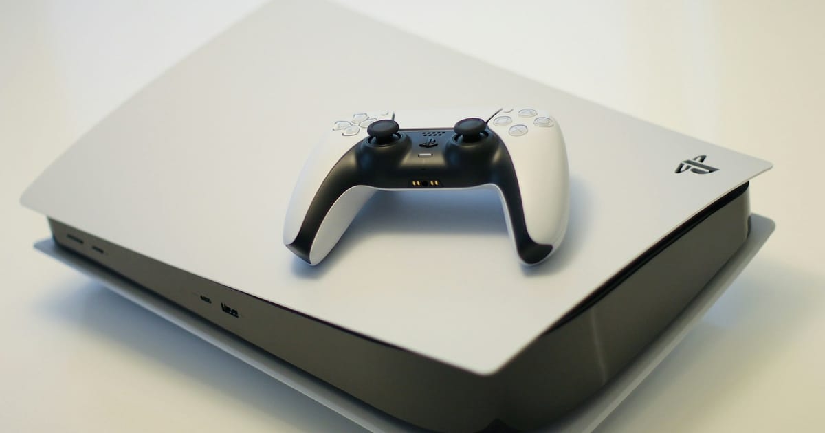 Una consola blanca de videojuegos junto a su control inalámbrico sobre una superficie clara.