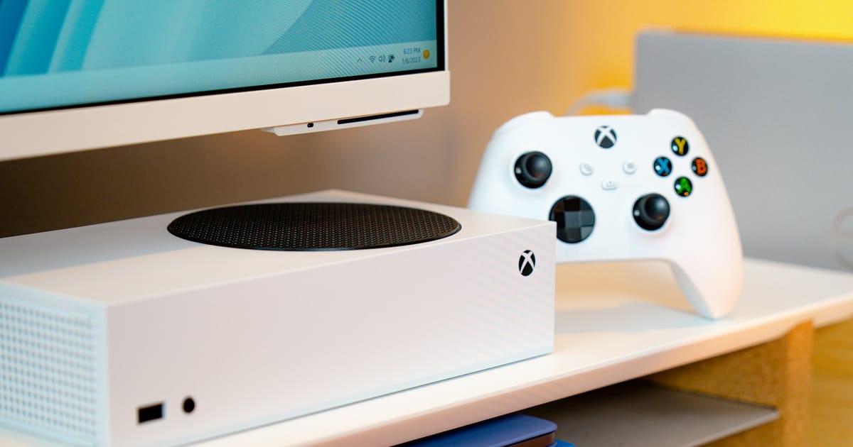 Una consola de videojuegos junto a un monitor sobre un escritorio.