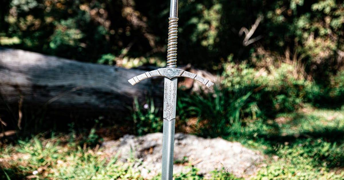 Una espada de metal clavada en el suelo de un bosque, junto a un tronco caído.