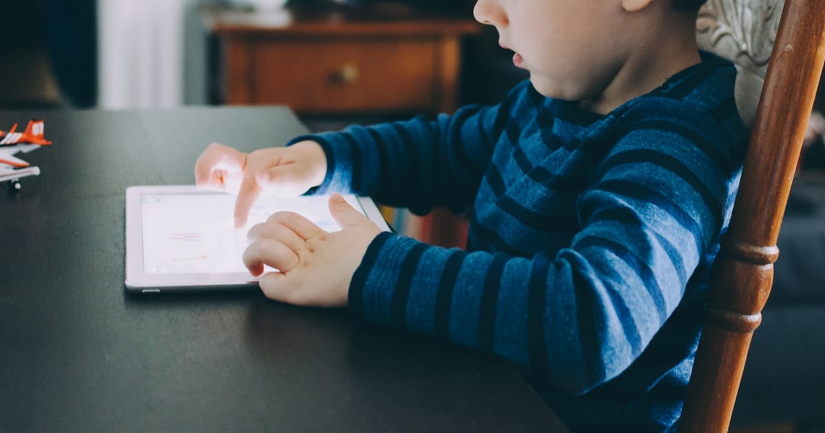 Un niño usa una tablet sentado a la mesa.