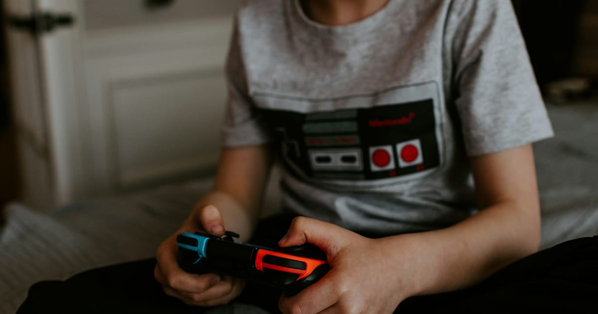 Un niño sentado en una cama mientras juega con un dispositivo portátil.