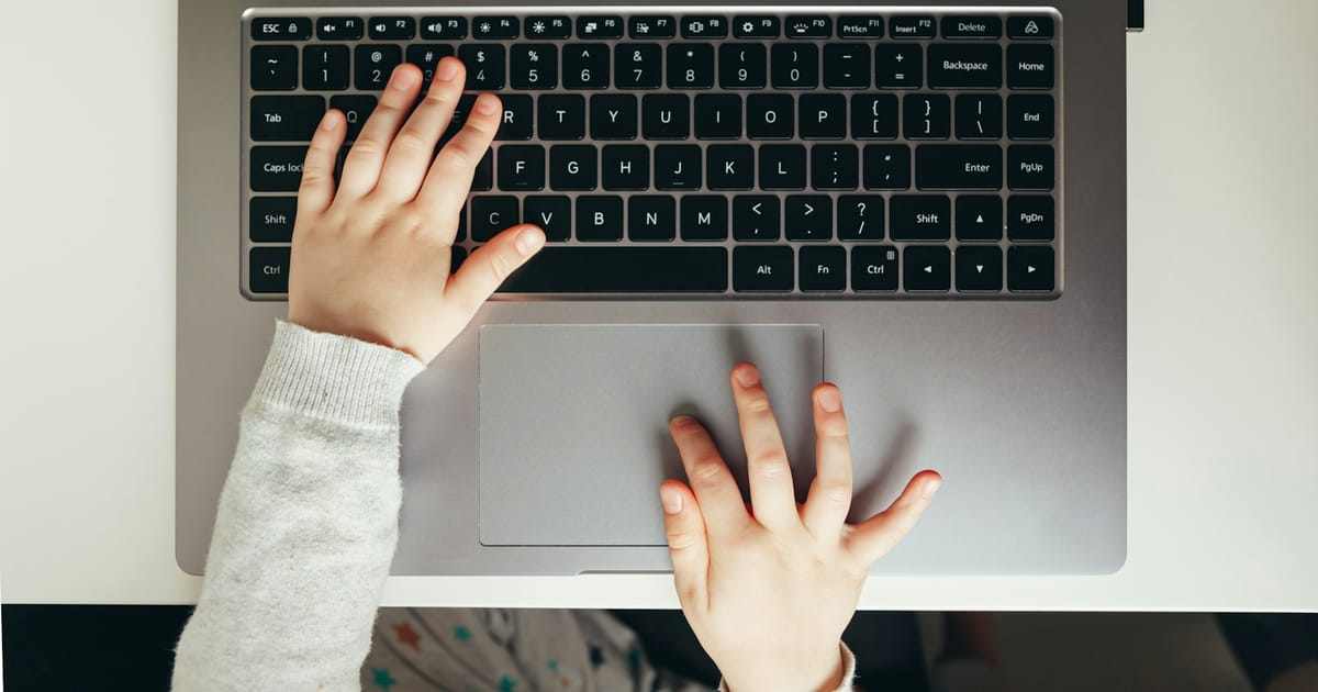 Las manos de un niño sobre el teclado y el panel táctil de una laptop.