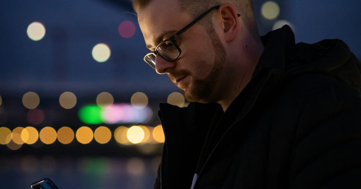 Un hombre mira la pantalla de su celular de noche, con el rostro iluminado por la luz.